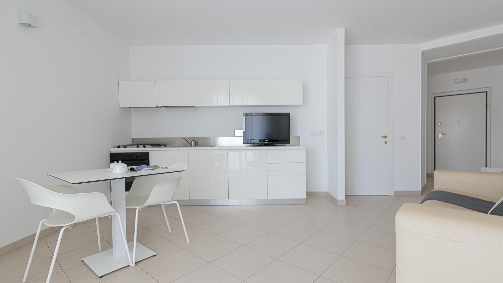 A compact kitchen with white cabinets, a black TV, and a dining area with white chairs.