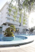 Un edificio moderno con area piscina, caratterizzata da un solarium piastrellato e una palma.
