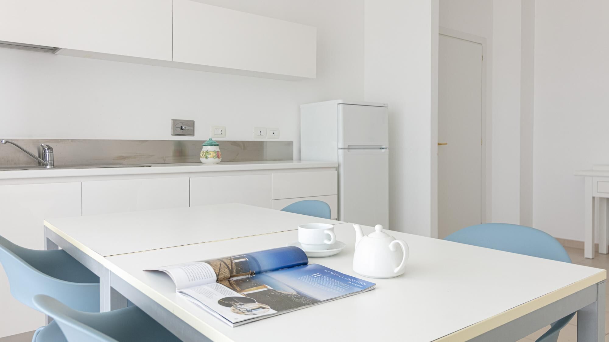 Una cocina moderna con armarios blancos, un refrigerador, un lavamanos y una mesa de comedor con sillas.