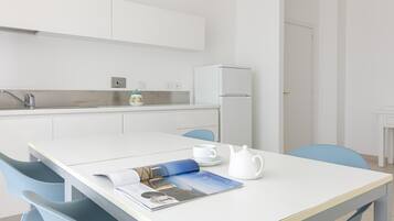 Una cocina moderna con armarios blancos, un refrigerador, un lavamanos y una mesa de comedor con sillas.