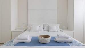Hotelkamer met een groot bed, wit beddengoed, een blauwe mat en een geweven mand.