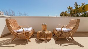 Twee rieten loungestoelen met kussens op een betegeld terras, met een decoratieve lantaarn in het midden.