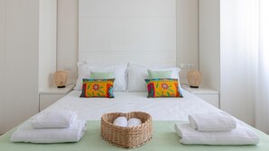 A neatly made bed with white linens, two decorative pillows with colorful patterns, a wicker basket with white towels, and two wall-mounted lamps. - Residenza Excelsior 603 (Vasto)