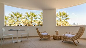 A room with two large windows overlooking palm trees, a white table with chairs, and two wicker chairs. - Residenza Excelsior 603 (Vasto)