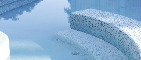 Una piscina cristalina con borde de azulejos y escalones que bajan al agua.
