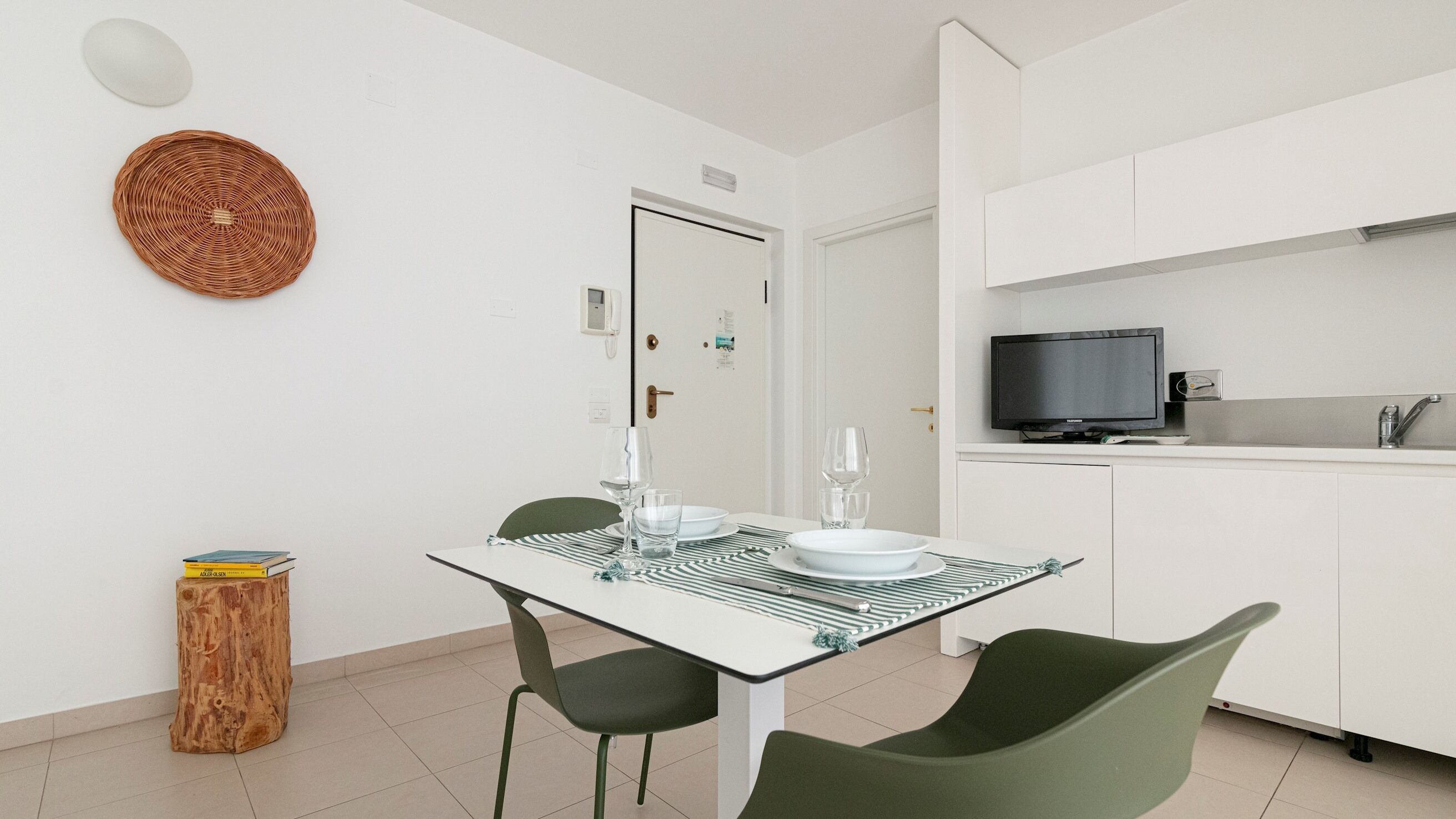 A modern kitchen with a TV, white cabinets, and a dining area with a glass table and chairs.