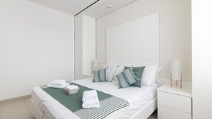 Una moderna camera d'hotel con un letto rifatto, biancheria a righe verdi e bianche, due lampade da comodino e un comodino bianco.