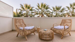 Two wicker lounge chairs with cushions, a small round table, and a decorative item on a tiled terrace with palm trees in the background. - Residenza Excelsior 605 (Vasto)