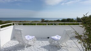 Un balcon avec deux fauteuils en osier, des coussins blancs et une vue sur la mer.