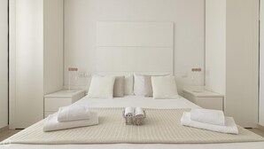 Une chambre à coucher au style minimaliste, avec un grand lit, deux tables de chevet, une lampe fixée au mur et une lampe de chevet.