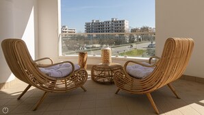 Un balcone con due sedie in vimini e un tavolino rotondo, affaccia su un panorama urbano con edifici e una strada.