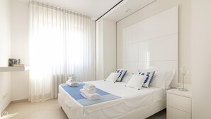 Una camera d'albergo moderna con un letto rifatto, un comodino e un'ampia finestra con tende leggere.