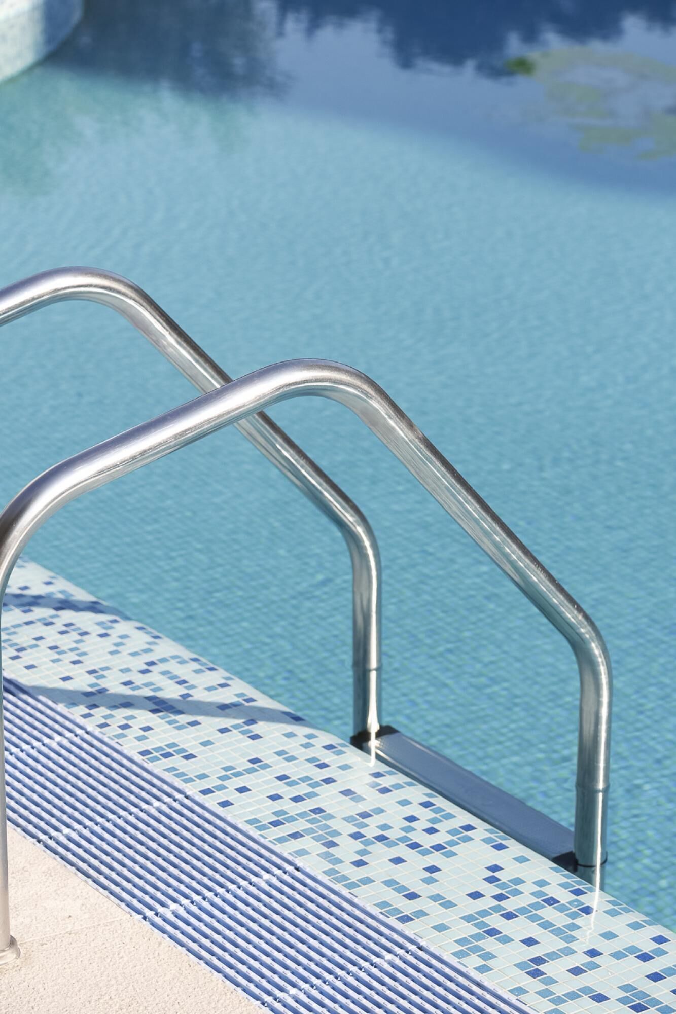 Una escalera metálica para la piscina con un borde de azulejos azules.