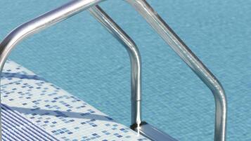Una escalera metálica para la piscina con un borde de azulejos azules.