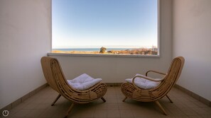 Two wicker chairs with white cushions facing a large window overlooking a beach. - Residenza Excelsior 805 (Vasto)
