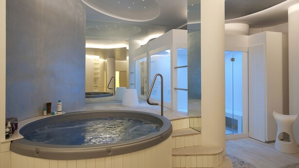 Un espace spa moderne doté d’un jacuzzi, de portes vitrées et d’un escalier menant à un niveau supérieur.