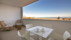 A balcony with a table and chairs, a wicker chair, and a view of the sea. - Residenza Excelsior 804 (Vasto)