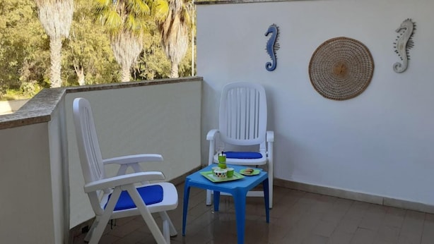 A balcony with two white chairs and a small table, a woven mat, and decorative wall art. - Le Barchette 8 - Primo Piano (Lecce)