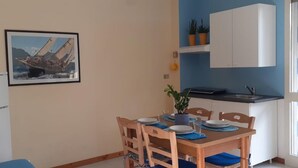 A dining area with a table set for four, a refrigerator, a kitchen area with cabinets, and a window with curtains. - Le Barchette 8 - Primo Piano (Lecce)