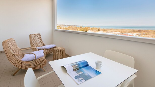 Ein Balkon mit Korbstühlen und einem Tisch, der Blick auf einen Strand und das Meer bietet.