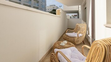 Un balcone con mobili in vimini, tra cui una sedia e un tavolino rotondo con teiera e tazza.