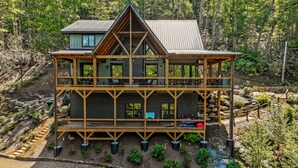 A multi-story wooden cabin with a balcony on each floor, surrounded by a forested landscape. - New Home on South Toe River, Pet Friendly (Burnsville)