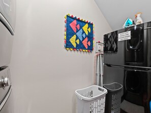 Una cocina con refrigerador, lavadora y un colorido edredón colgado en la pared.