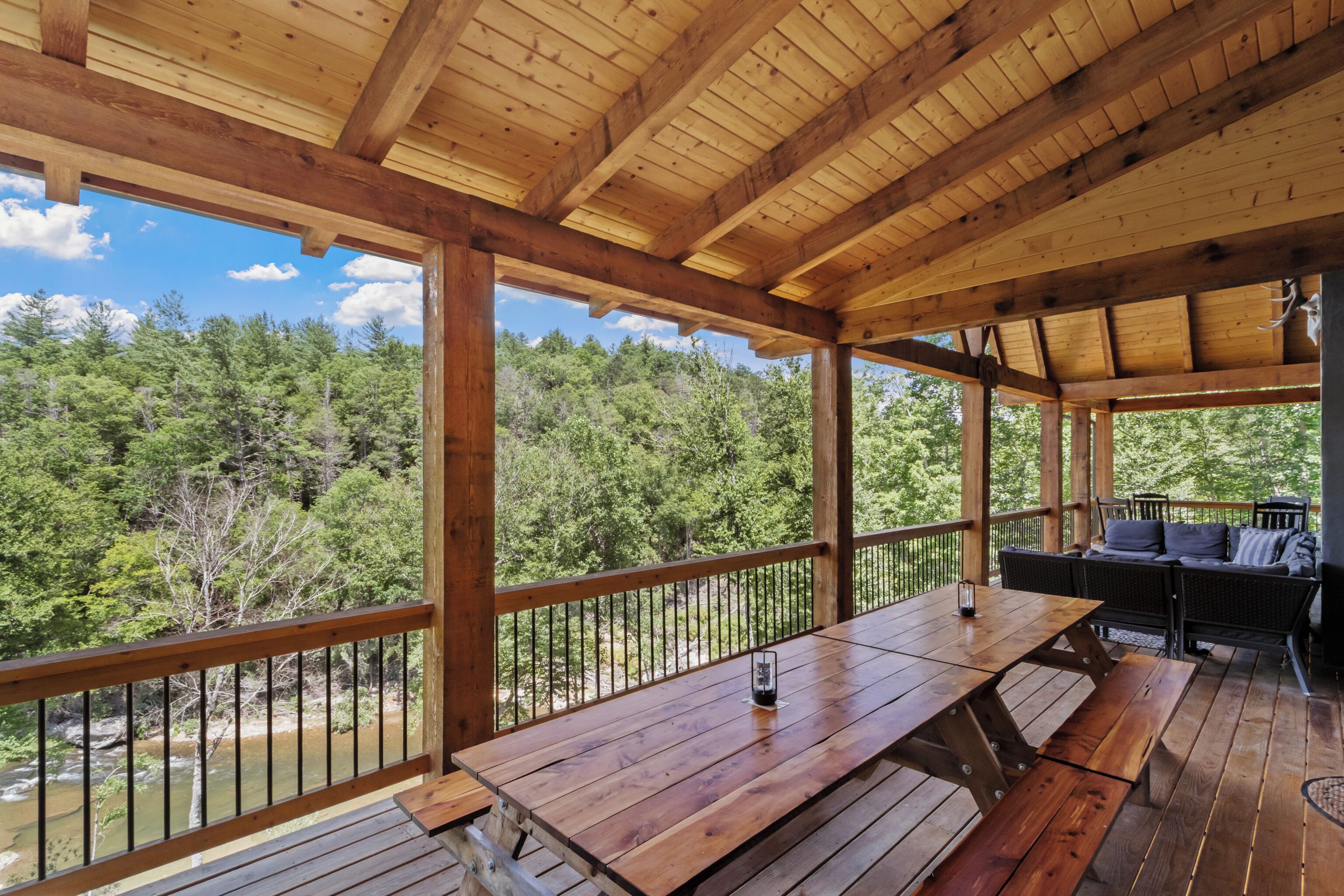 Une terrasse en bois avec une table et des bancs, donnant sur une zone boisée et un plan d’eau.