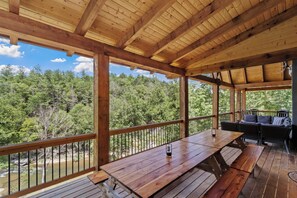 A wooden deck with a table and benches, overlooking a forested area and a body of water.