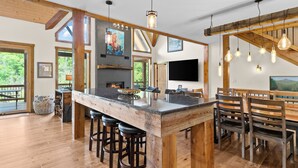 A spacious kitchen with a large island, wooden beams, and a fireplace. - New Home on South Toe River, Pet Friendly (Burnsville)