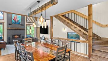 Un vaste espace de vie comprenant une grande table à manger en bois, des sièges confortables, une cheminée et un escalier.