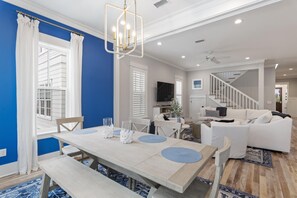 A spacious living room with a dining area, a staircase, and a TV mounted on the wall.