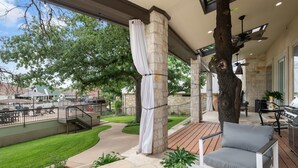 Un patio exterior techado con suelo de piedra, una mesa blanca y una silla gris.