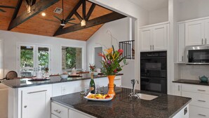 Una cocina moderna con armarios blancos, encimera de granito, horno empotrado y refrigerador de acero inoxidable.