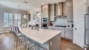 A modern kitchen with a large island, bar stools, stainless steel appliances, and a patterned backsplash.