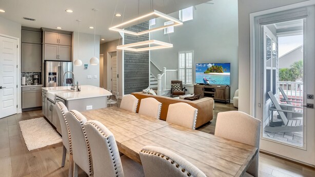 A modern kitchen with a central island, a dining area with a large table and chairs, and a living area with a sofa and TV.