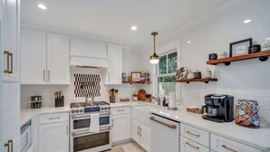 A modern kitchen with white cabinetry, a gas stove, a coffee maker, and decorative items on shelves.