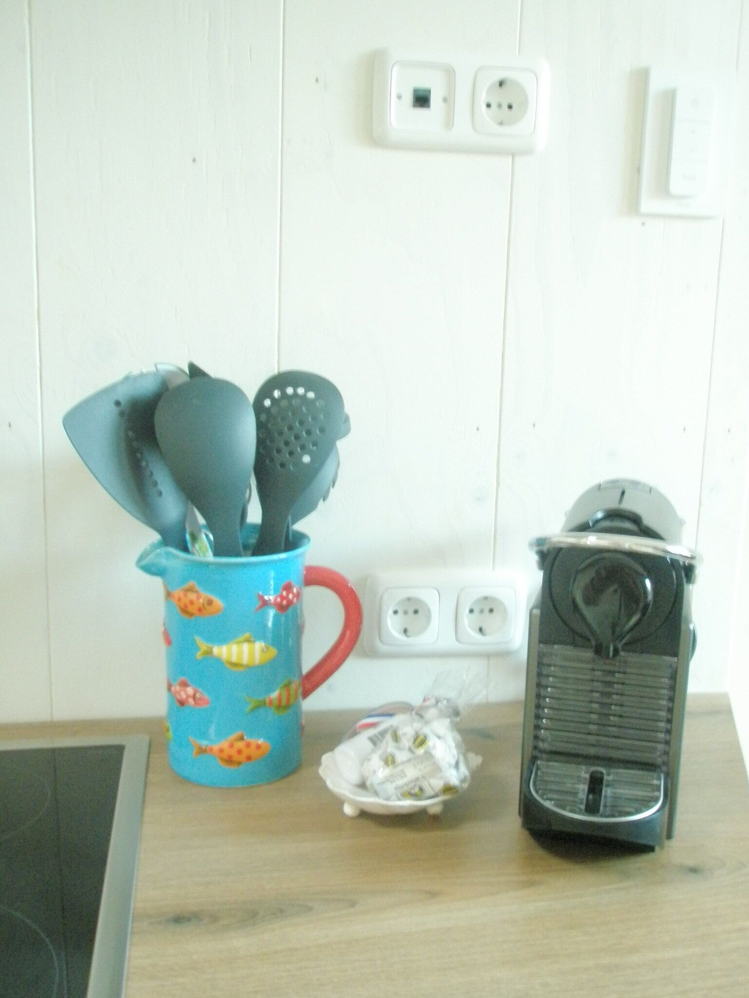 Un comptoir de cuisine avec une tasse bleue ornée de motifs de poissons, des ustensiles de cuisine, une petite assiette et une machine à café.