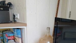 A living room with a wooden shelf holding books, a large bottle, and a remote control. A plant is in a woven basket on the floor. - Luxury apartment for beach/walking  3 minute walk to the beautiful sandy beach. (Egmond aan Zee)
