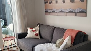 A modern living room with a grey sofa, a red table, and a large beach-themed painting on the wall. - Luxury apartment for beach/walking  3 minute walk to the beautiful sandy beach. (Egmond aan Zee)