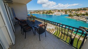 Een balkon met een tafel en stoelen met uitzicht op een kustplaatsje, helderblauw water en boten.
