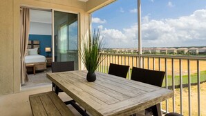 A balcony with a wooden table and chairs, a potted plant, and a view of a residential area.