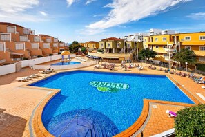 A large outdoor swimming pool with a sunbathing area and lounge chairs, surrounded by multi-story buildings.