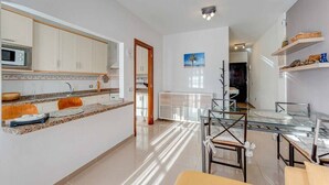 Une cuisine moderne avec des meubles blancs, un plan de travail en granit et une table à manger en verre.