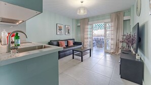 Un salon moderne avec un canapé, une table basse et un téléviseur. Il y a également un coin cuisine équipé d’un évier et d’un réfrigérateur.