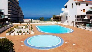 Un complexe hôtelier doté d’une grande piscine, offrant une vue sur la plage et présentant un bâtiment moderne.