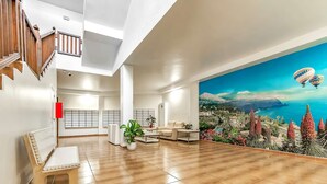 Un salon spacieux doté d’un plancher en bois, d’un canapé, d’une table basse et d’une grande fresque murale représentant un paysage côtier avec des montgolfières.