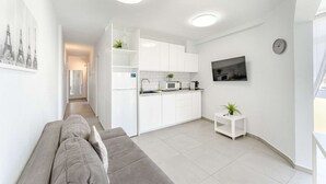A modern, compact living space with a kitchenette, a grey sofa, and a small side table with a plant. - Rising Sun Apartment in complex Las Terrazas (Adeje)
