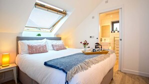 A bedroom with a skylight, a bed with pillows, a bedside table with a lamp, and a tray with items. - The Neyth (Mabe Burnthouse)