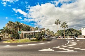 A hotel entrance with a curved road, palm trees, and a clear sky. - Moderno apartamento en el Parque Royal I (Adeje)